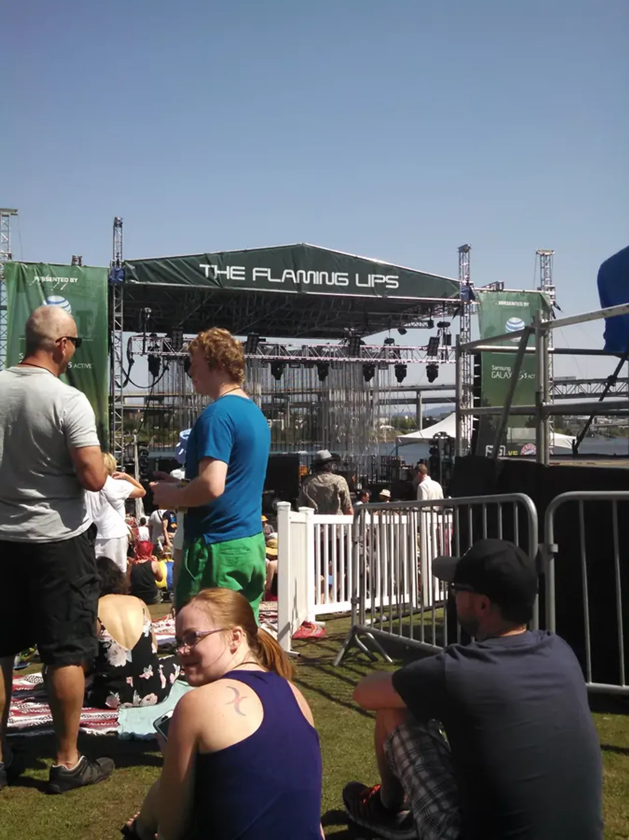 Sunny outdoor concert stage for The Flaming Lips with crowd relaxing on grass nearby.